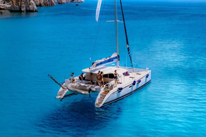 Sailboat on clear blue water near rocky cliffs with people on deck.
