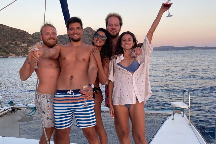 Five people on a boat deck, smiling and holding drinks at sunset.