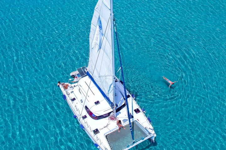 Aerial view of sailboat and person swimming in clear blue water.
