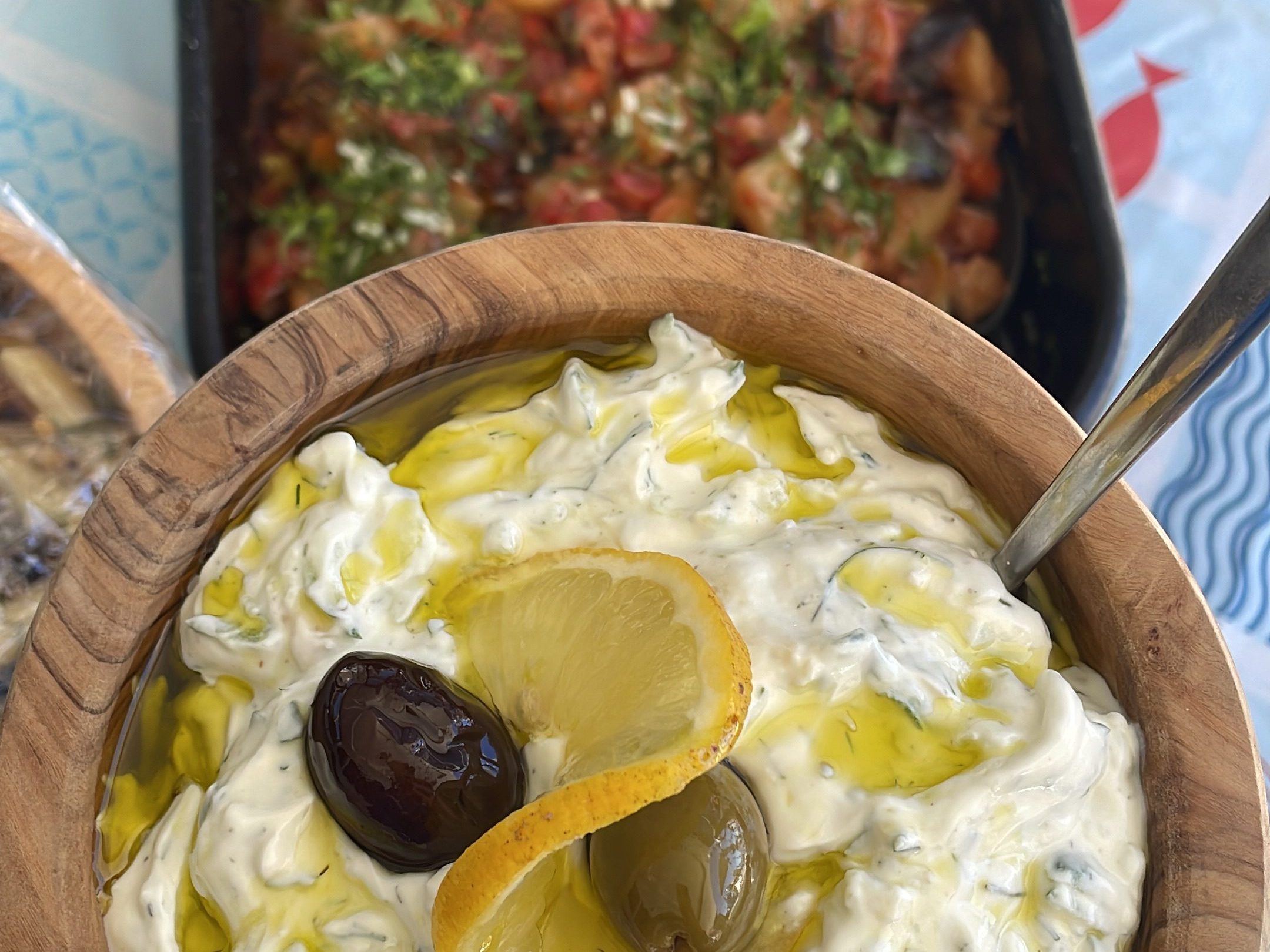 Bowl of creamy dip with olives and lemon slices, next to a tray of mixed vegetables.