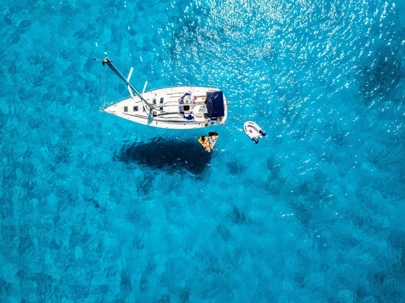 Aerial view of a sailboat and dinghy on clear turquoise water.