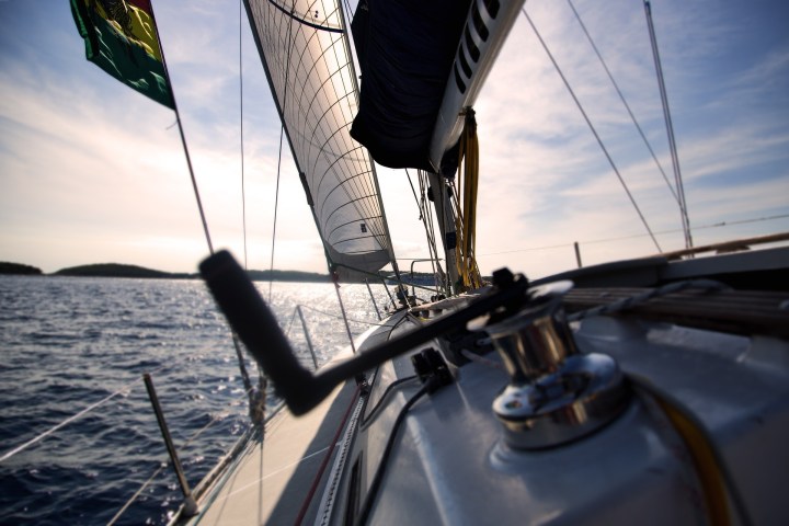 Sunset view from deck of a sailing yacht with sails raised on open water.