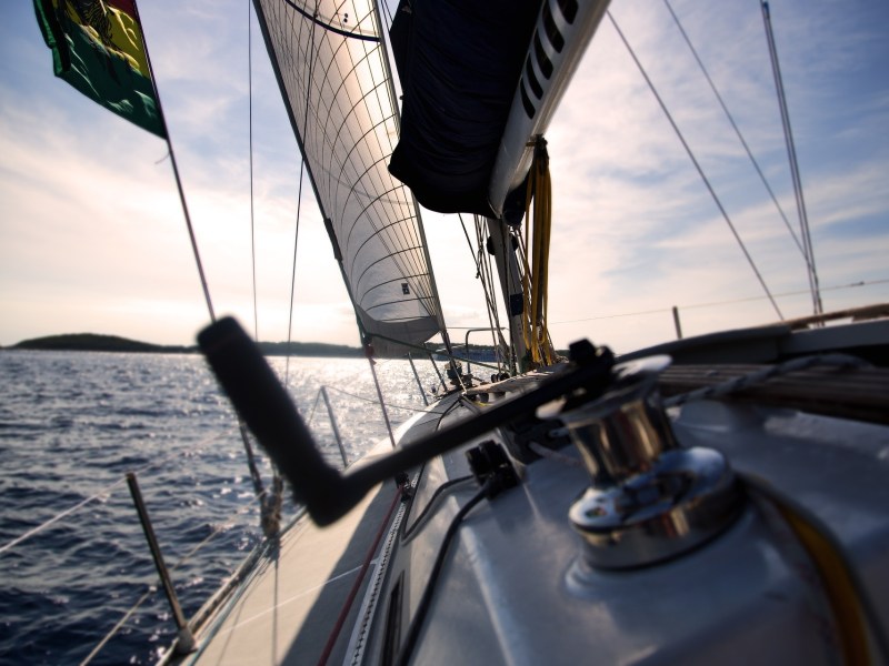 Sunset view from deck of a sailing yacht with sails raised on open water.