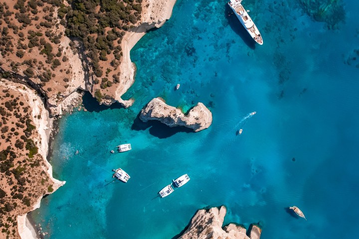 Aerial view of boats in a turquoise lagoon with rocky cliffs and an arch.