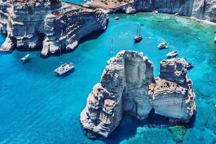Aerial view of sailboats near white cliffs in clear blue water.