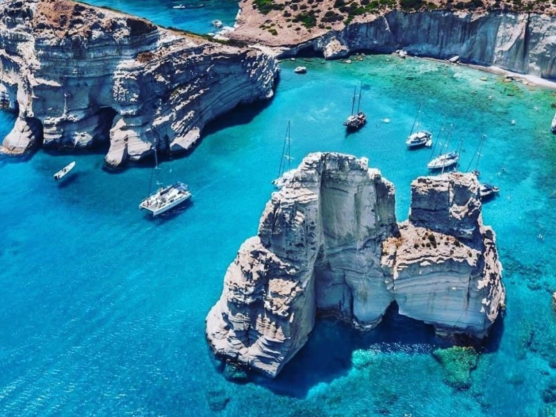 Aerial view of sailboats near white cliffs in clear blue water.