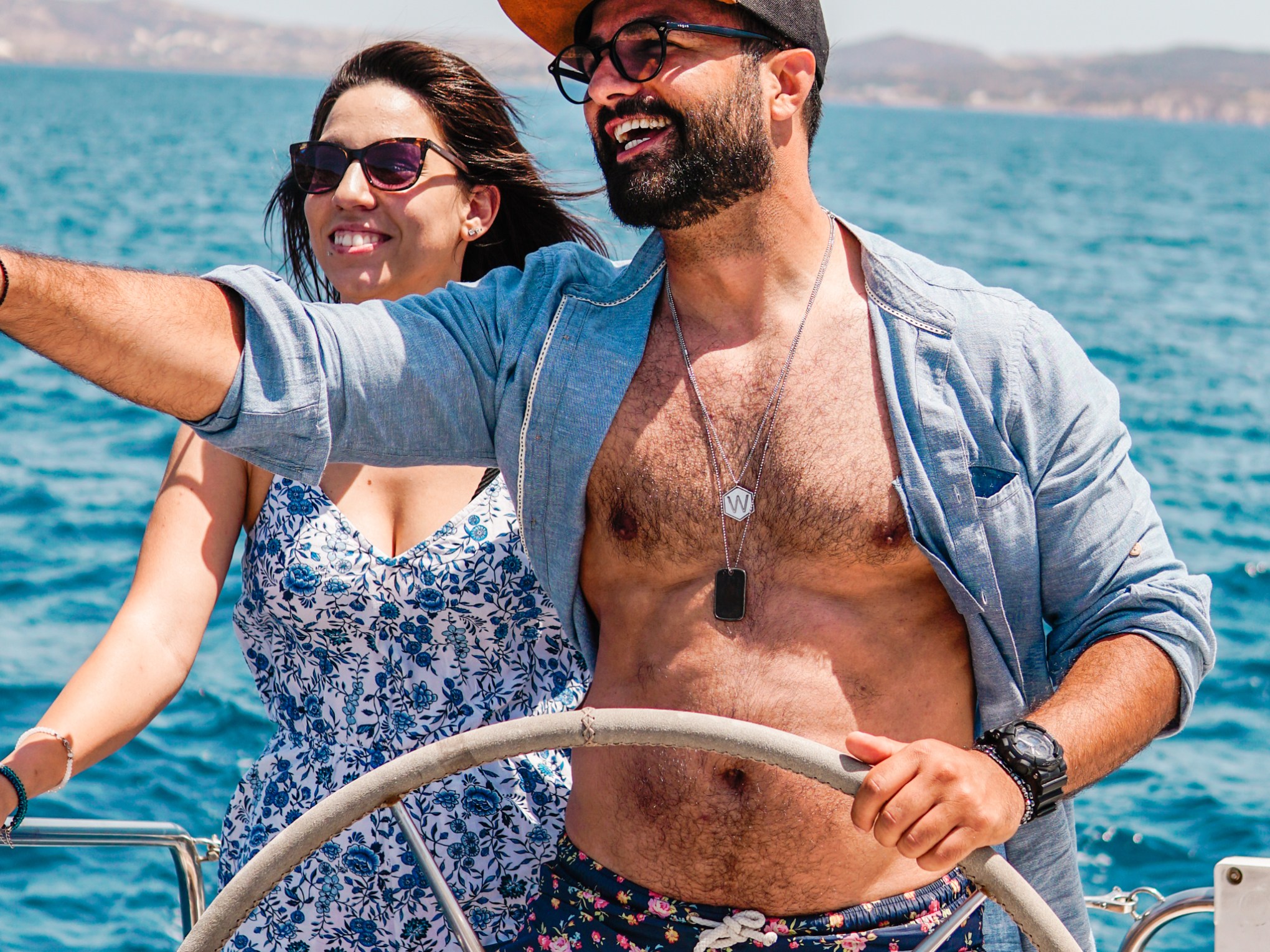 Man and woman smiling on a sailboat in the ocean on a sunny day.