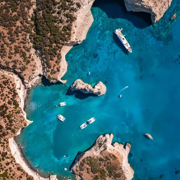 Aerial view of boats in a blue cove surrounded by rocky cliffs.