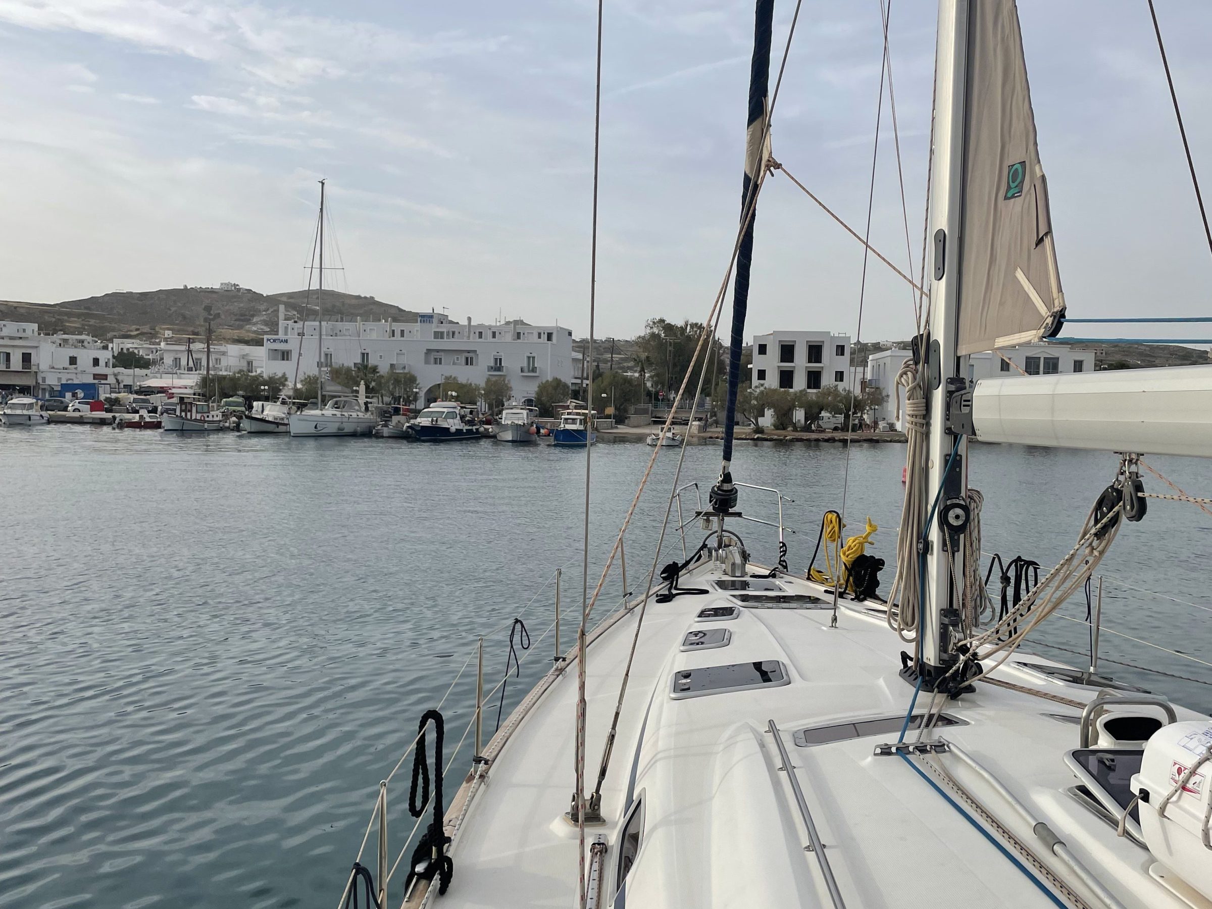 View from a sailboat deck towards a harbor with buildings and calm water.
