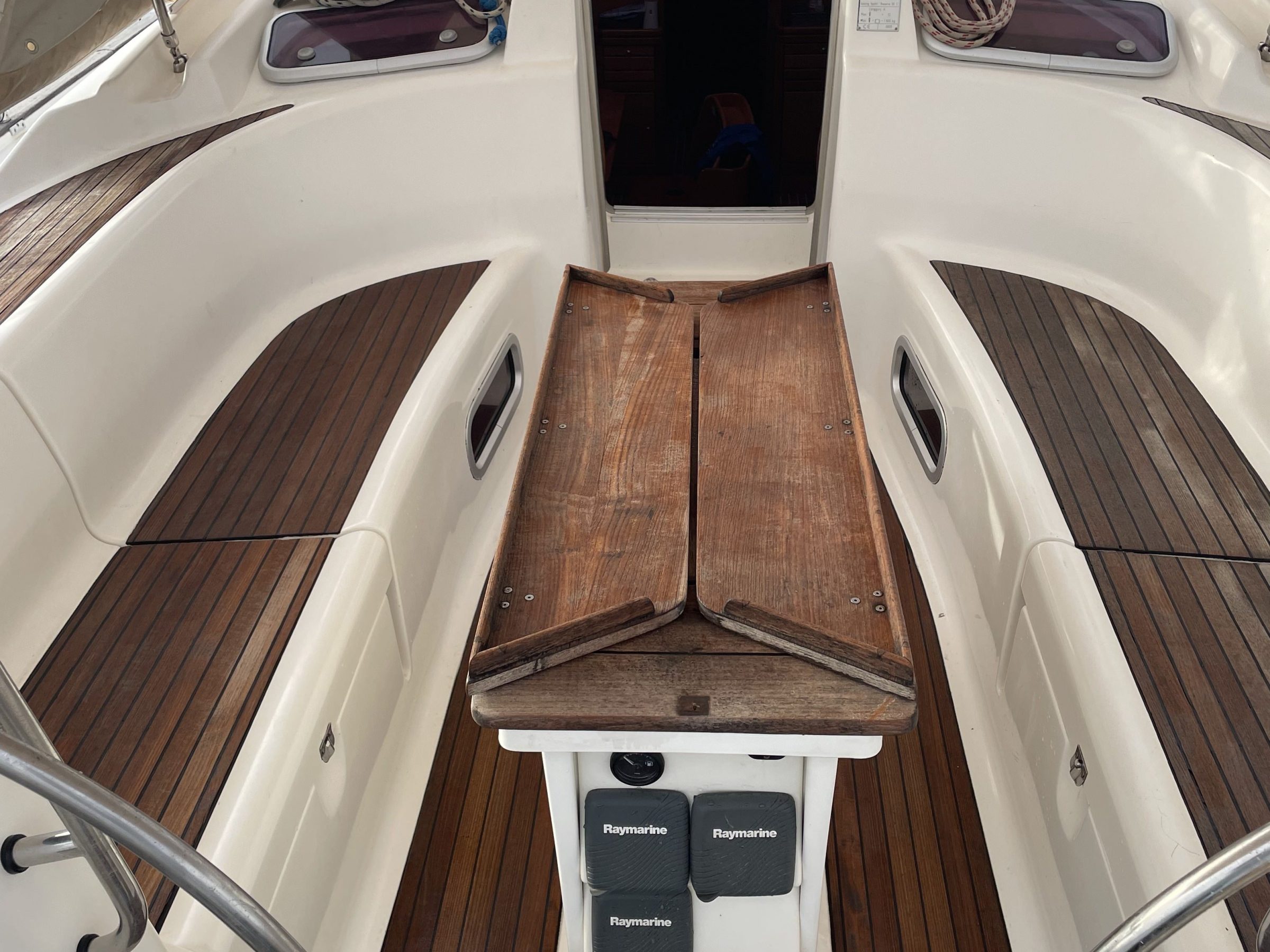 Boat cockpit with wooden flooring, folding table, and nautical equipment.