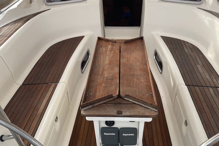 Boat cockpit with wooden flooring, folding table, and nautical equipment.