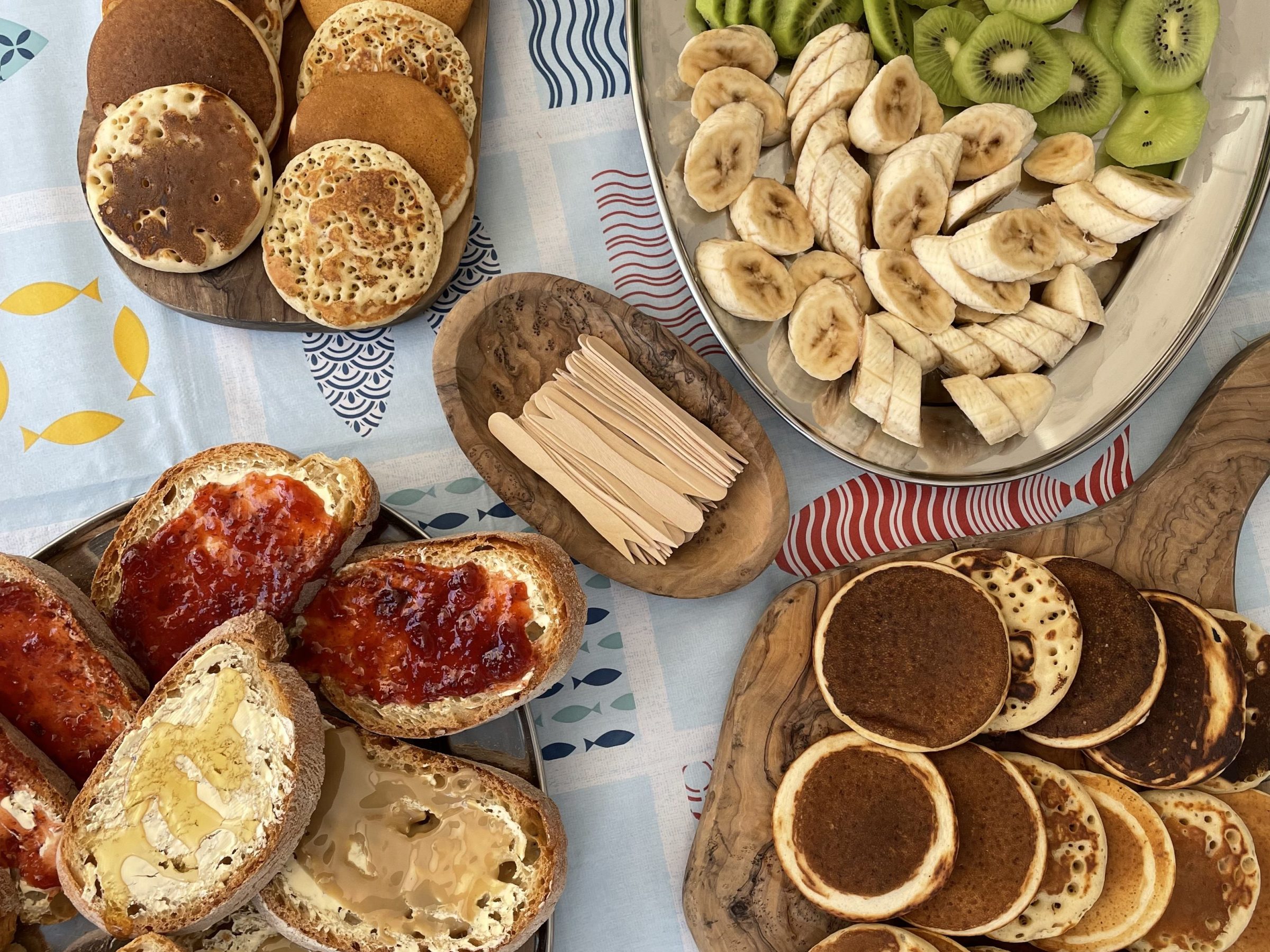 Assorted pancakes, toasts with spreads, and sliced fruits on a table.