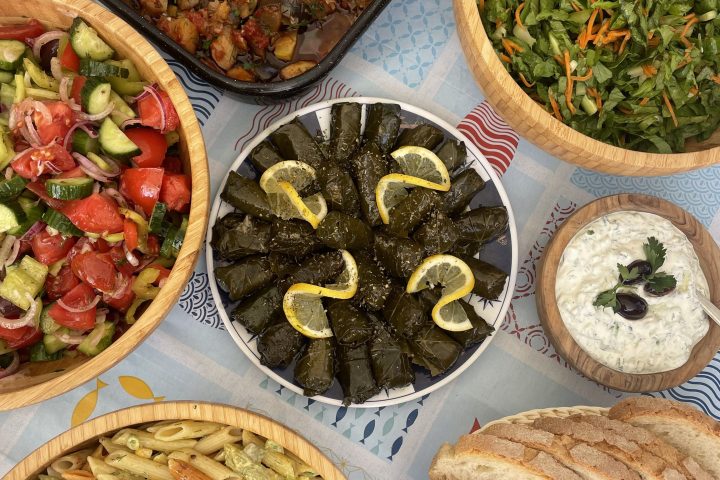 Assorted Mediterranean dishes including salads, vine leaves, and bread on a table.