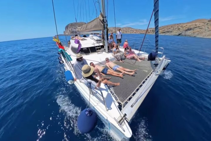 People relaxing on a catamaran sailboat in clear blue waters under a sunny sky.