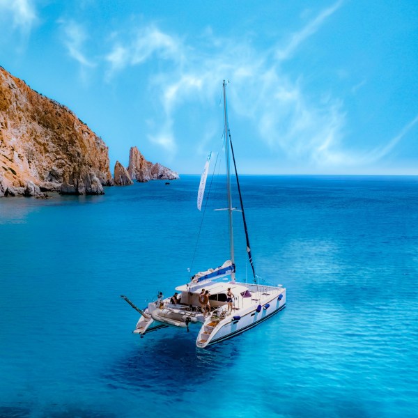 Catamaran with people in blue sea near rocky coastline under clear sky.