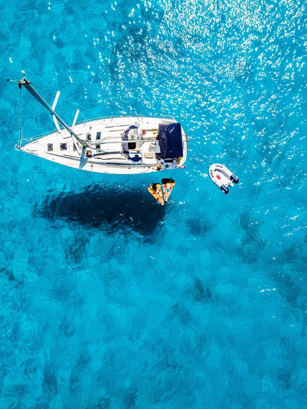 Aerial view of sailboat on clear blue water with nearby kayak and inflatable raft.