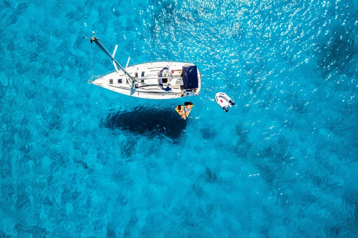Aerial view of sailboat on clear blue water with nearby kayak and inflatable raft.
