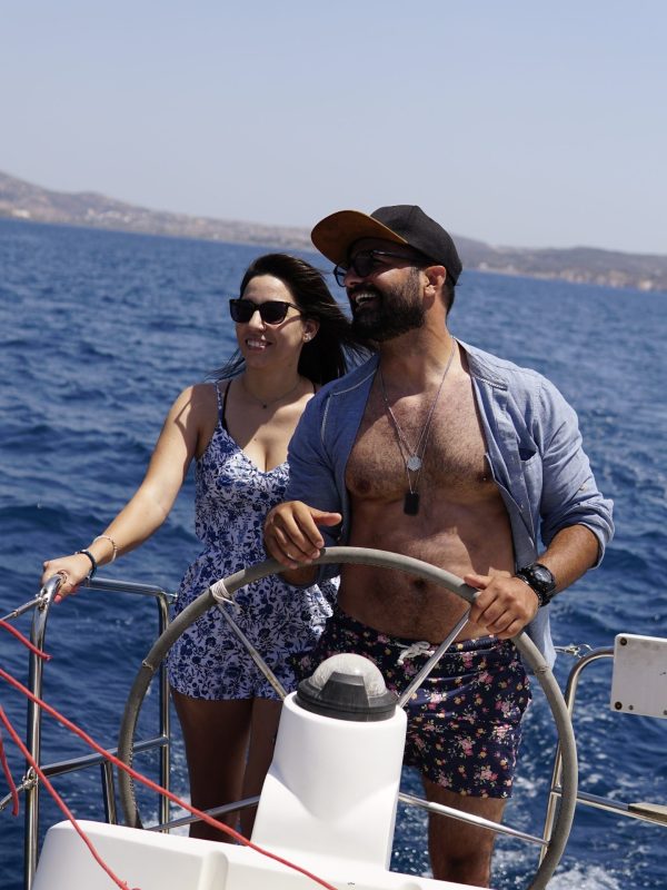 A couple steering a boat on a sunny day with a blue sea and distant shoreline.