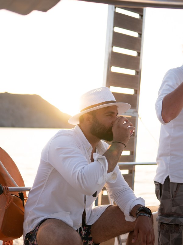 Man in white hat and shirt drinks on a boat at sunset.