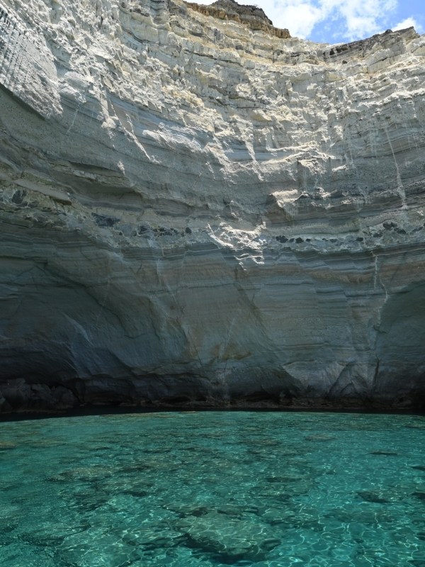 Rocky cliff over turquoise water with part of a boat and blue flag visible.