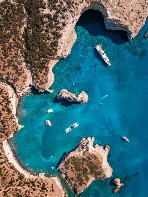 Aerial view of blue water bay with boats, rocky cliffs, and a cave.