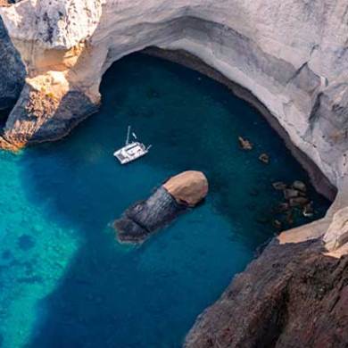 Aerial view of a sailboat in a coastal cave with clear blue water.