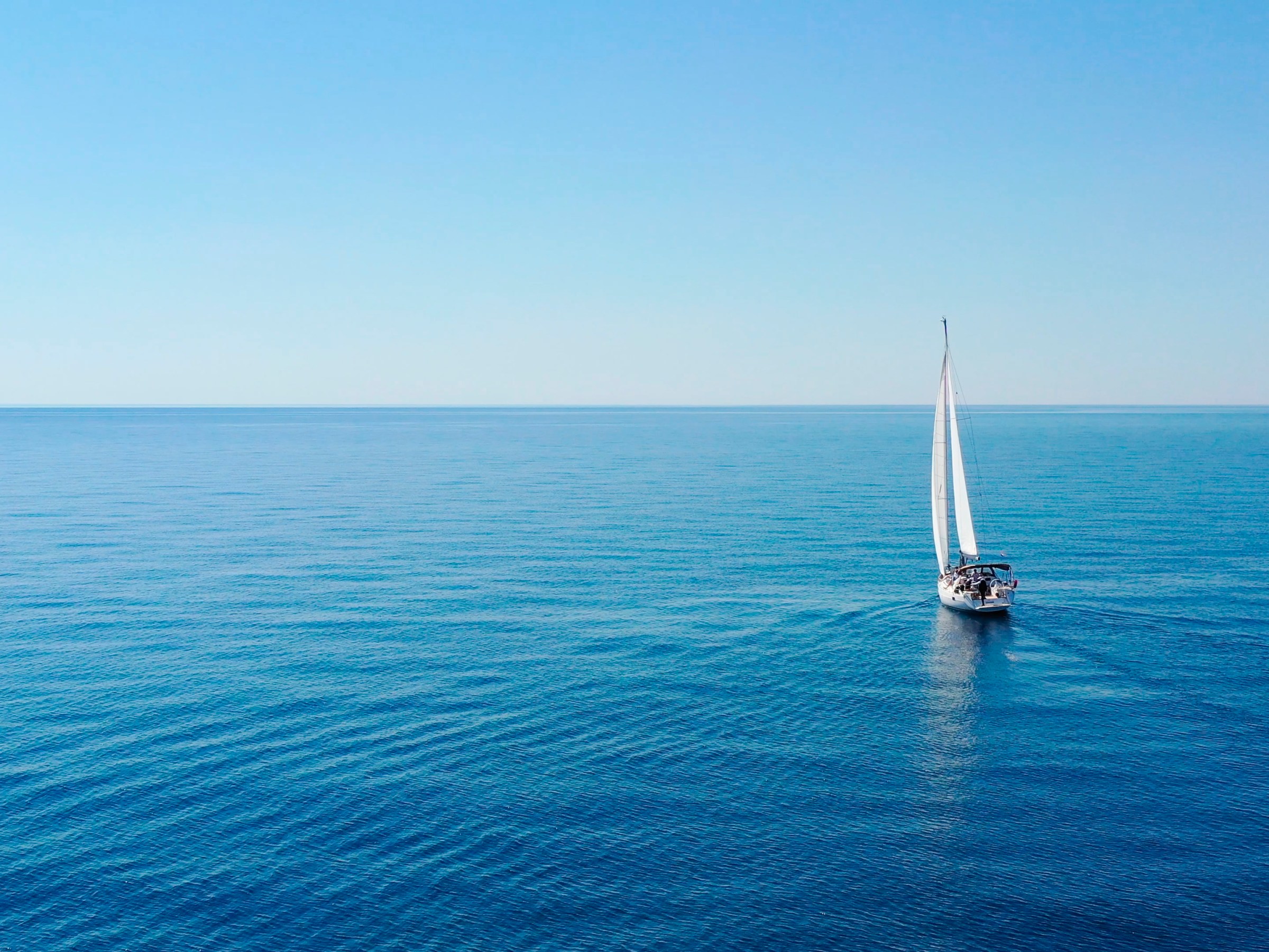 Sailboat on calm blue ocean under clear sky.