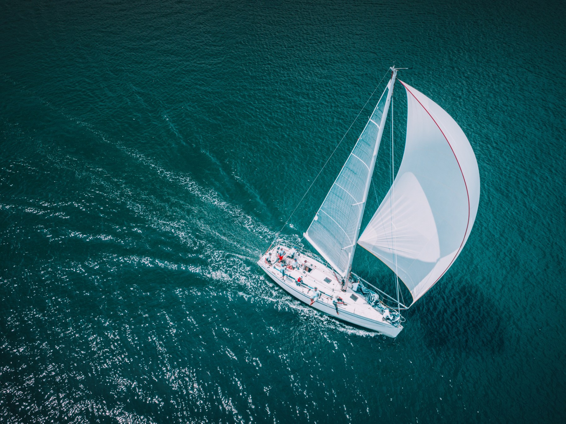 Aerial view of sailboat with white sails cruising on deep blue ocean.