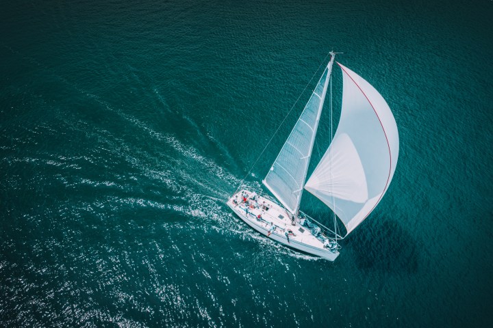 Aerial view of sailboat with white sails cruising on deep blue ocean.