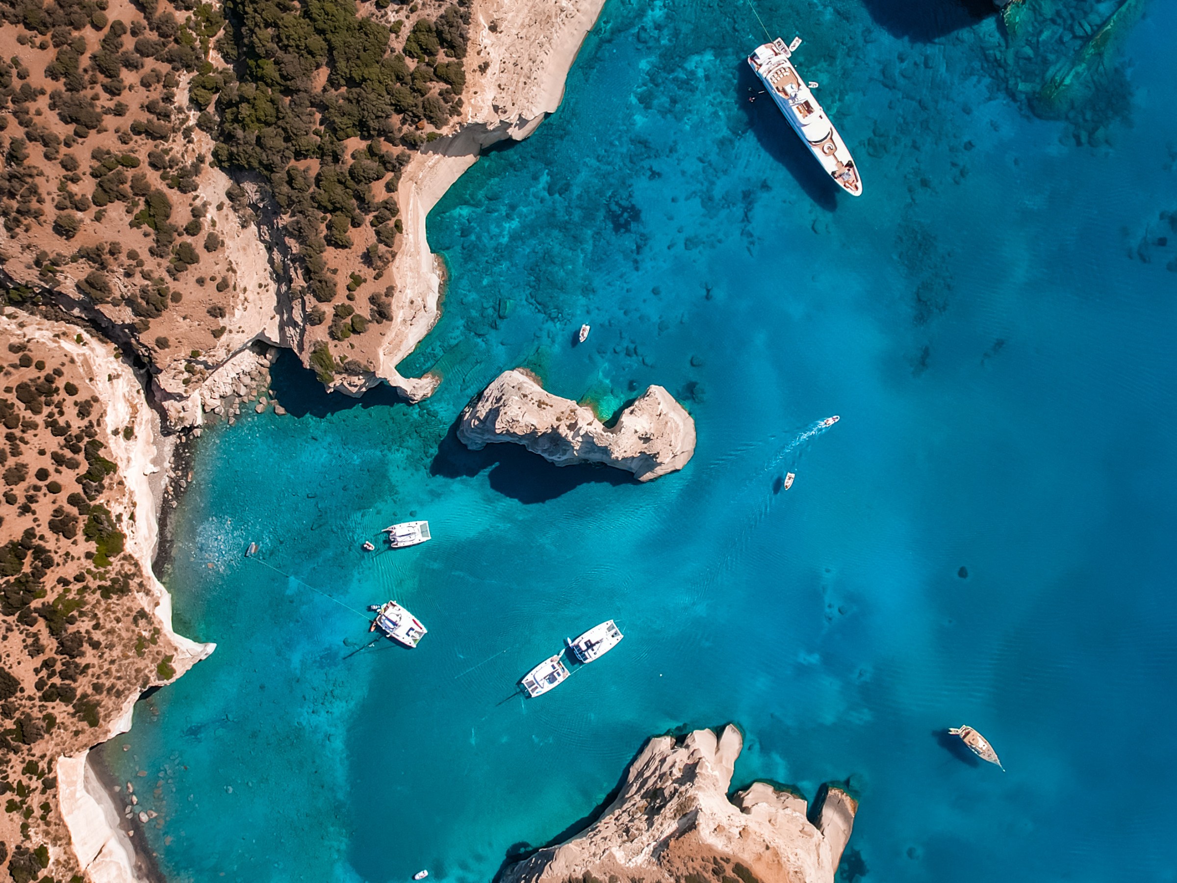 Aerial view of boats in a clear blue bay surrounded by rocky cliffs.