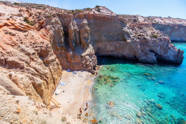 Secluded beach with turquoise water, surrounded by rocky cliffs and a few people sunbathing.