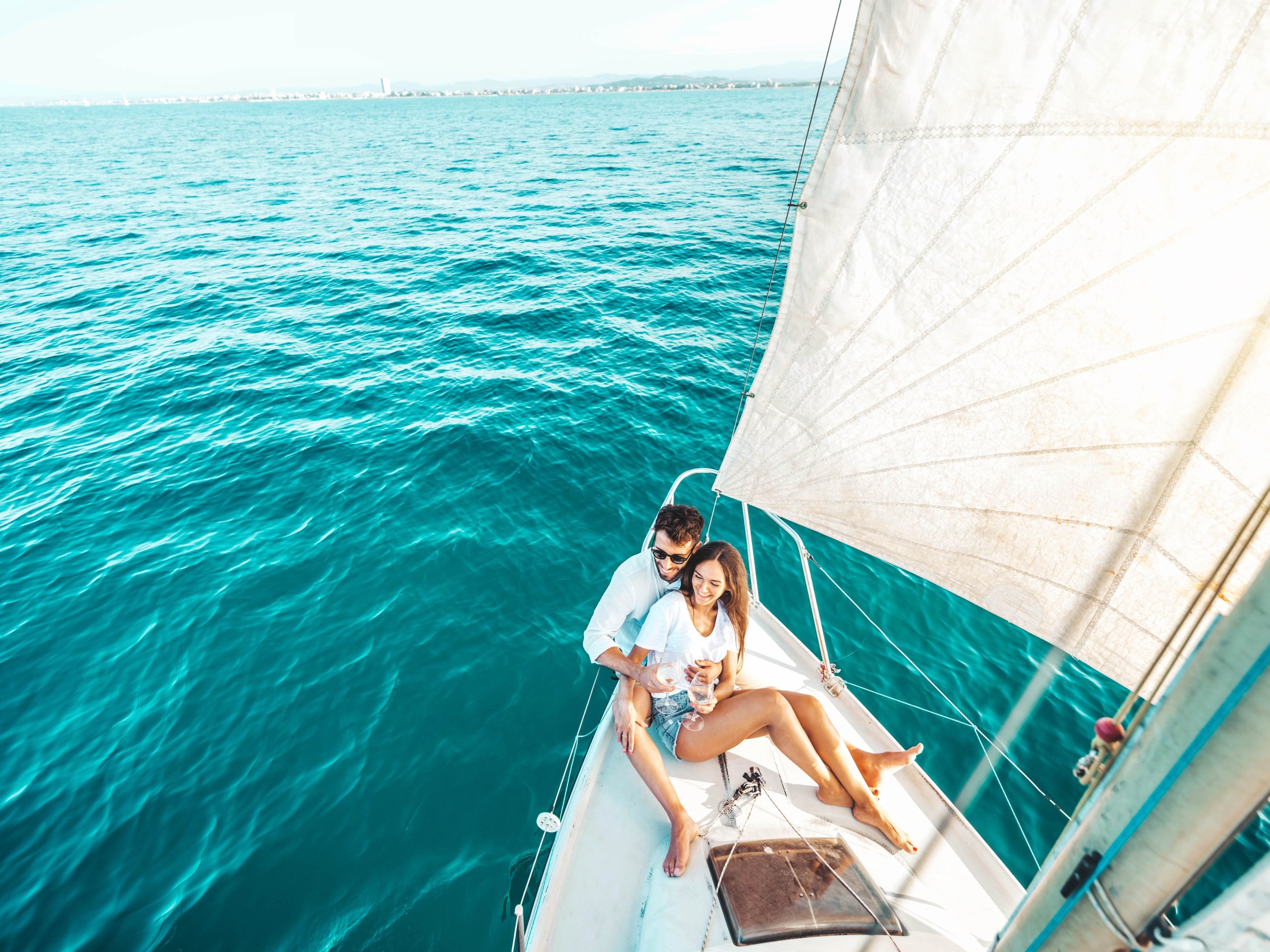 Couple on a sailboat in bright blue ocean, enjoying a sunny day.