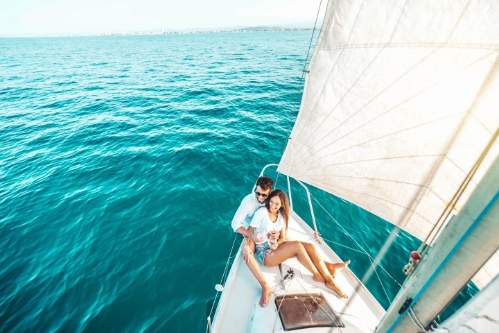 Couple on a sailboat in bright blue ocean, enjoying a sunny day.