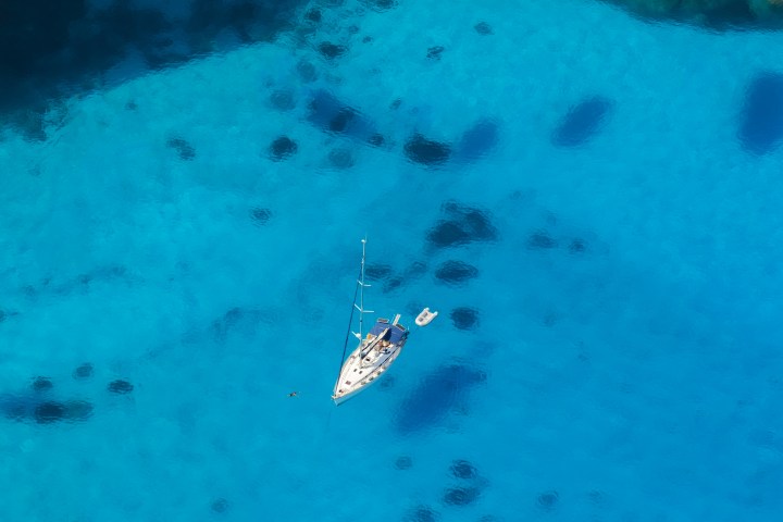 Aerial view of a sailboat on clear blue water, casting dark shadows.